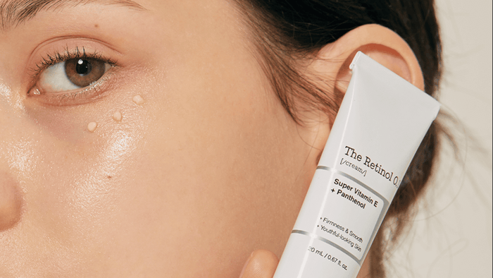 Närbild av en kvinna som applicerar en hudvårdsprodukt, med små droppar av krämen på hennes kind. Produkten är märkt 