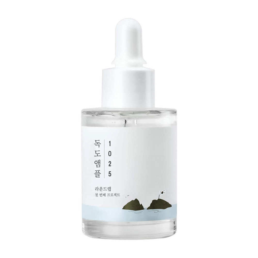 Een doorzichtige fles met 1025 Dokdo Ampoule gezichtsserum, versierd met een minimalistisch zeethema, op een witte achtergrond.