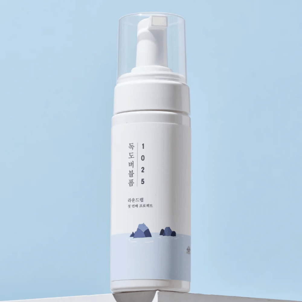  Het product is een "1025 Dokdo Bubble Foam" van ROUND LAB, verpakt in een witte pompflacon met een minimalistisch ontwerp. Het is bedoeld voor diepe reiniging van het gezicht zonder irritatie.