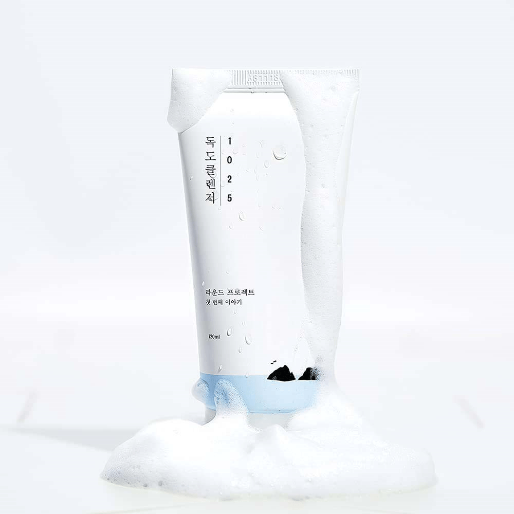 1025 Dokdo Cleanser in witte tube bedekt met schuim, met waterparels en schuim rond de onderkant, vrijstaand tegen lichte achtergrond.