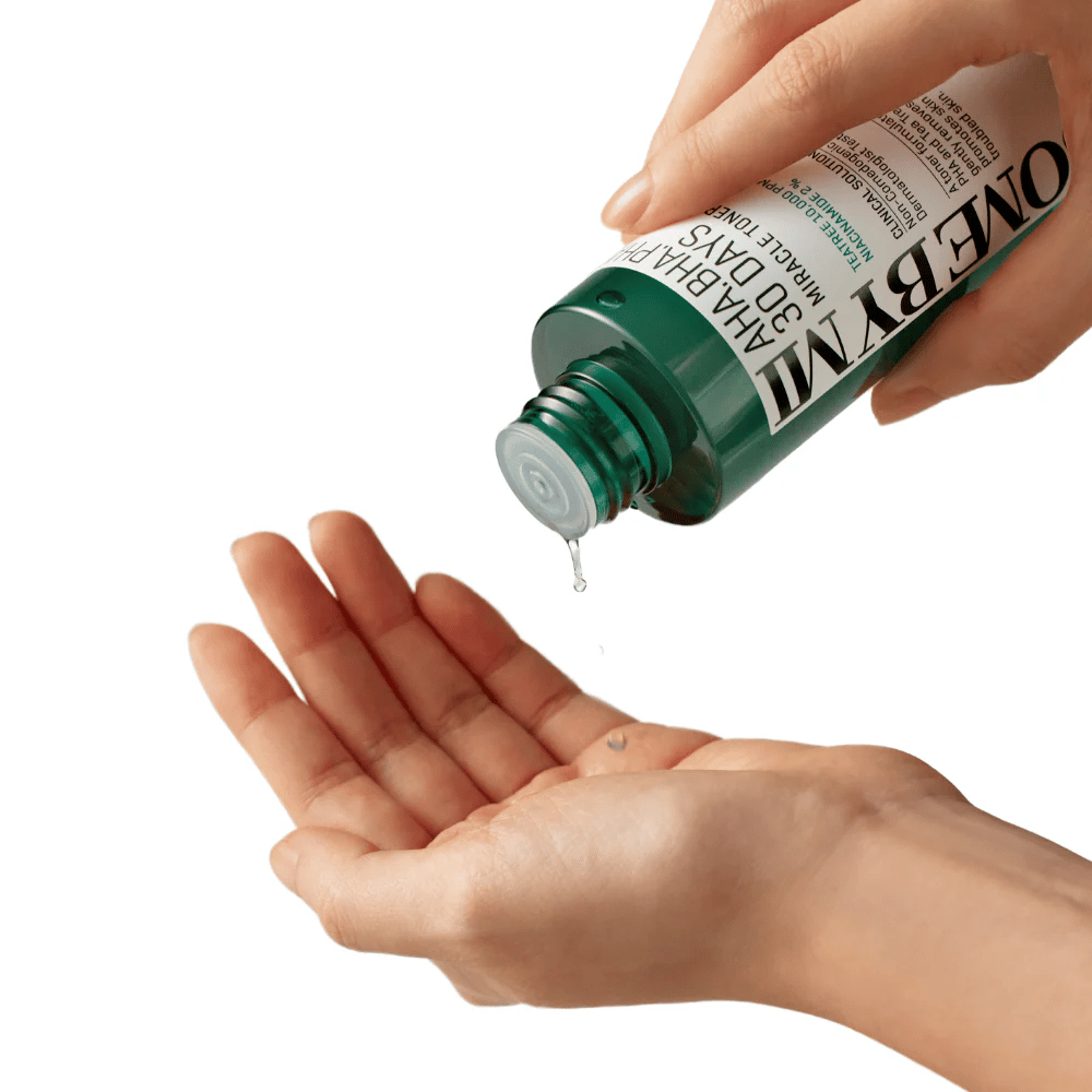 Een hand houdt een groene fles met de tekst "AHA, BHA, PHA 30 Days Miracle Toner" en perst een heldere vloeistof in de handpalm van de andere hand, klaar voor gebruik.