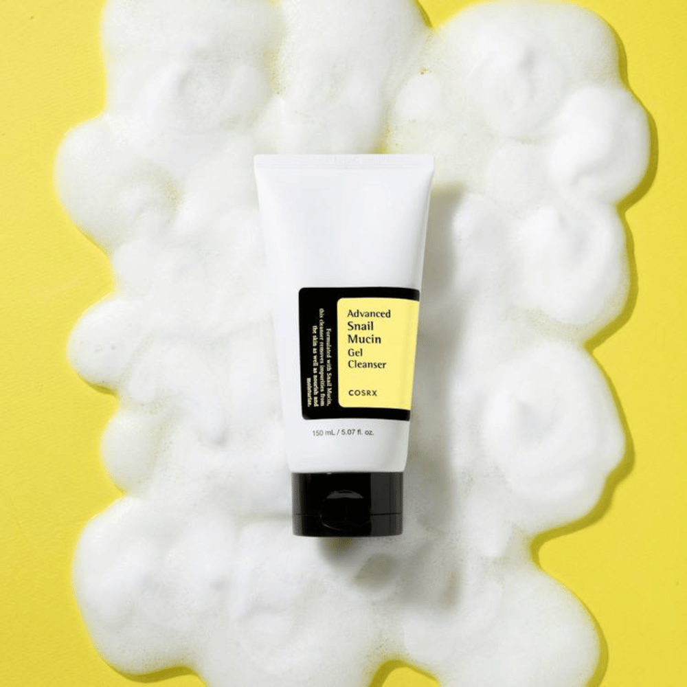 COSRX Advanced Snail Mucin Gel Cleanser 150 ml omgeven door rijkelijk schuim op gele achtergrond – milde Koreaanse gezichtsreiniger met snail mucin voor hydratatie en glans.