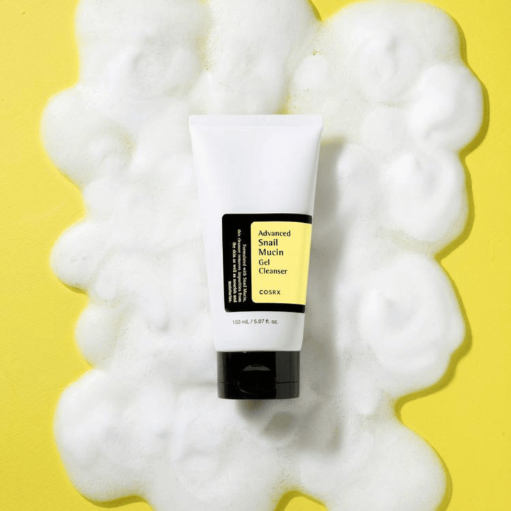 COSRX Advanced Snail Mucin Gel Cleanser 150 ml omgeven door rijkelijk schuim op gele achtergrond – milde Koreaanse gezichtsreiniger met snail mucin voor hydratatie en glans.