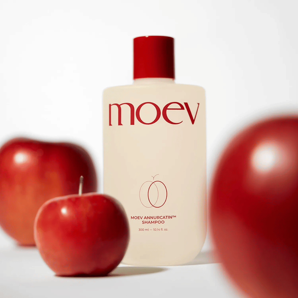 MOEV Annurcatin Shampoo geplaatst tussen rode appels – geïnspireerd door de antioxidanten van de Annurca-appel die sterker, gezonder en glanzender haar geven.