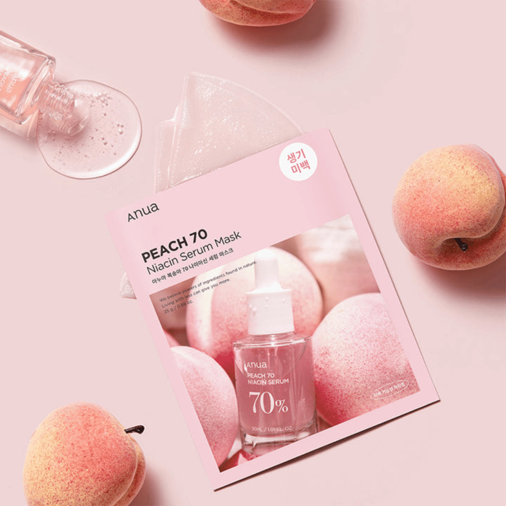 Een afbeelding van Anua PEACH 70 Niacin Serum Mask, omringd door perziken en een fles serum. De afbeelding heeft een zachte roze achtergrond, wat de roze verpakking aanvult en het product en de ingrediënten benadrukt.