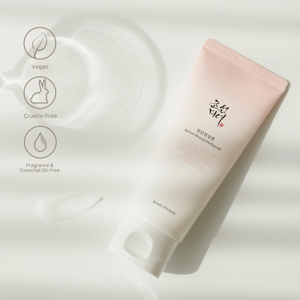 Een tube met Apricot Blossom Peeling Gel ligt op een reflecterend oppervlak met pictogrammen die aangeven dat het product veganistisch, diervriendelijk en vrij van geur en etherische oliën is.
