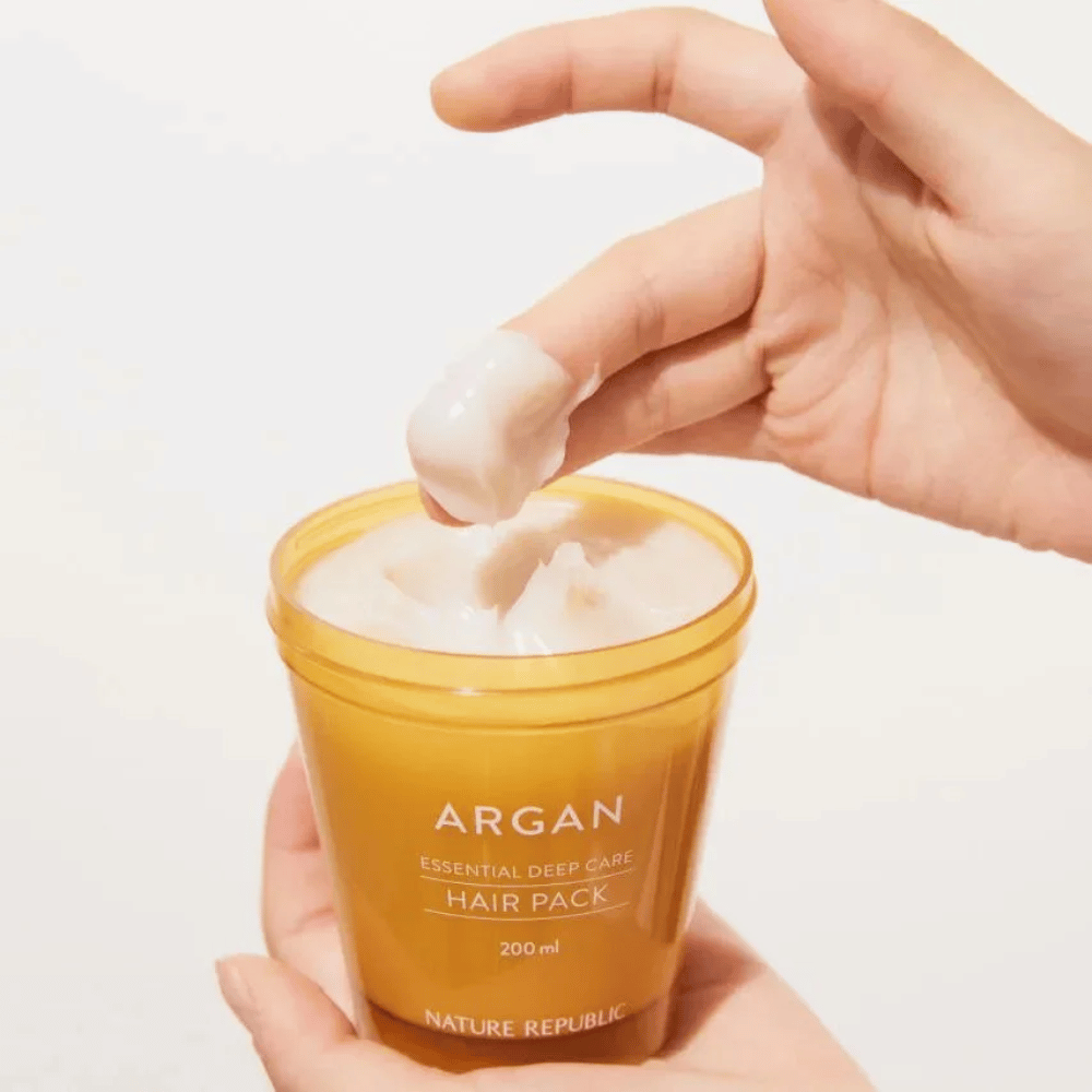 Hand neemt de romige formule uit Nature Republic Argan Essential Moisture Repairing Hair Mask – intensieve voeding voor droog haar.