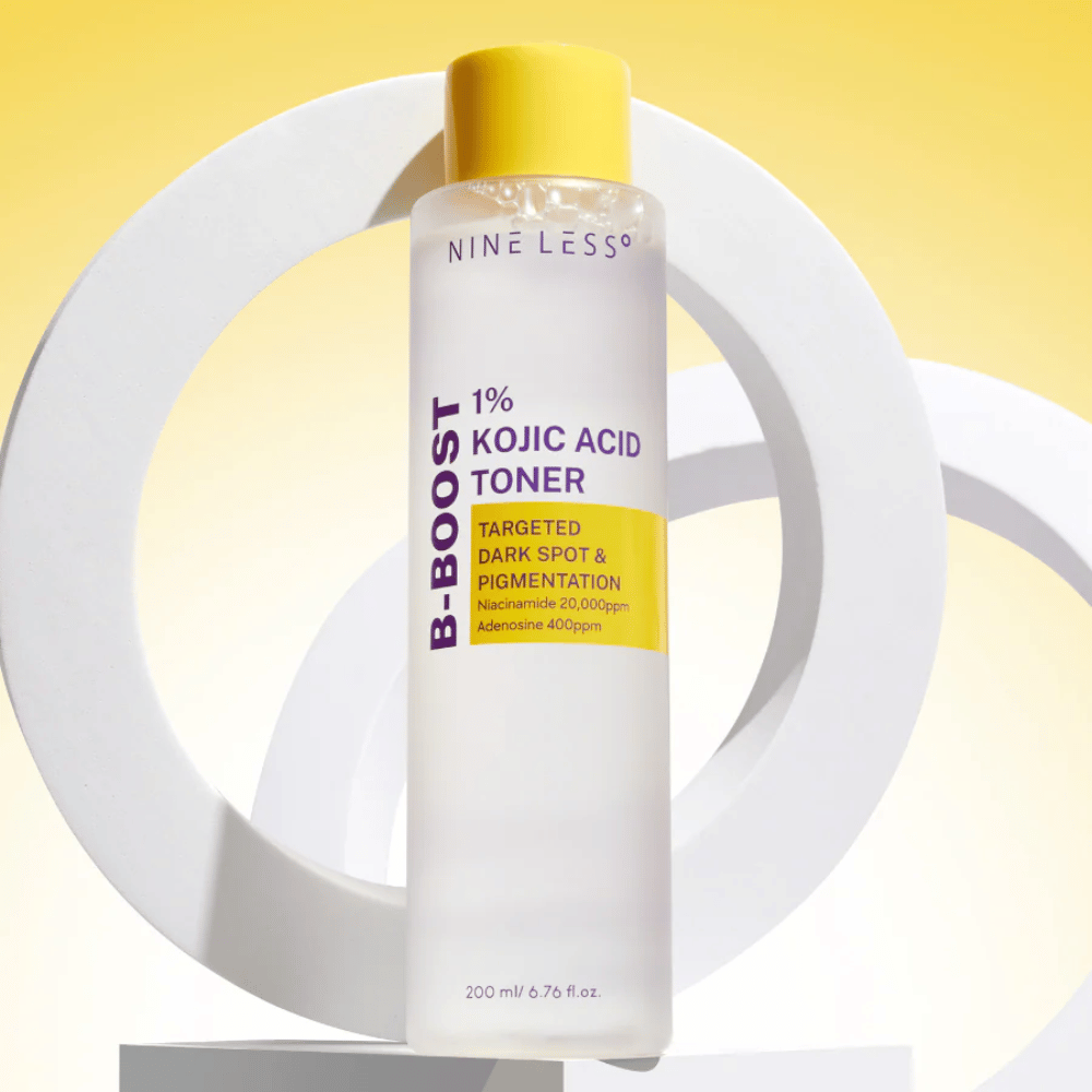 NINE LESS B-Boost 1% Kojic Acid Toner staande tegen een gele achtergrond met de tekst "Targeted Dark Spot & Pigmentation". Huidtint-egaliserende toner met niacinamide en adenosine.