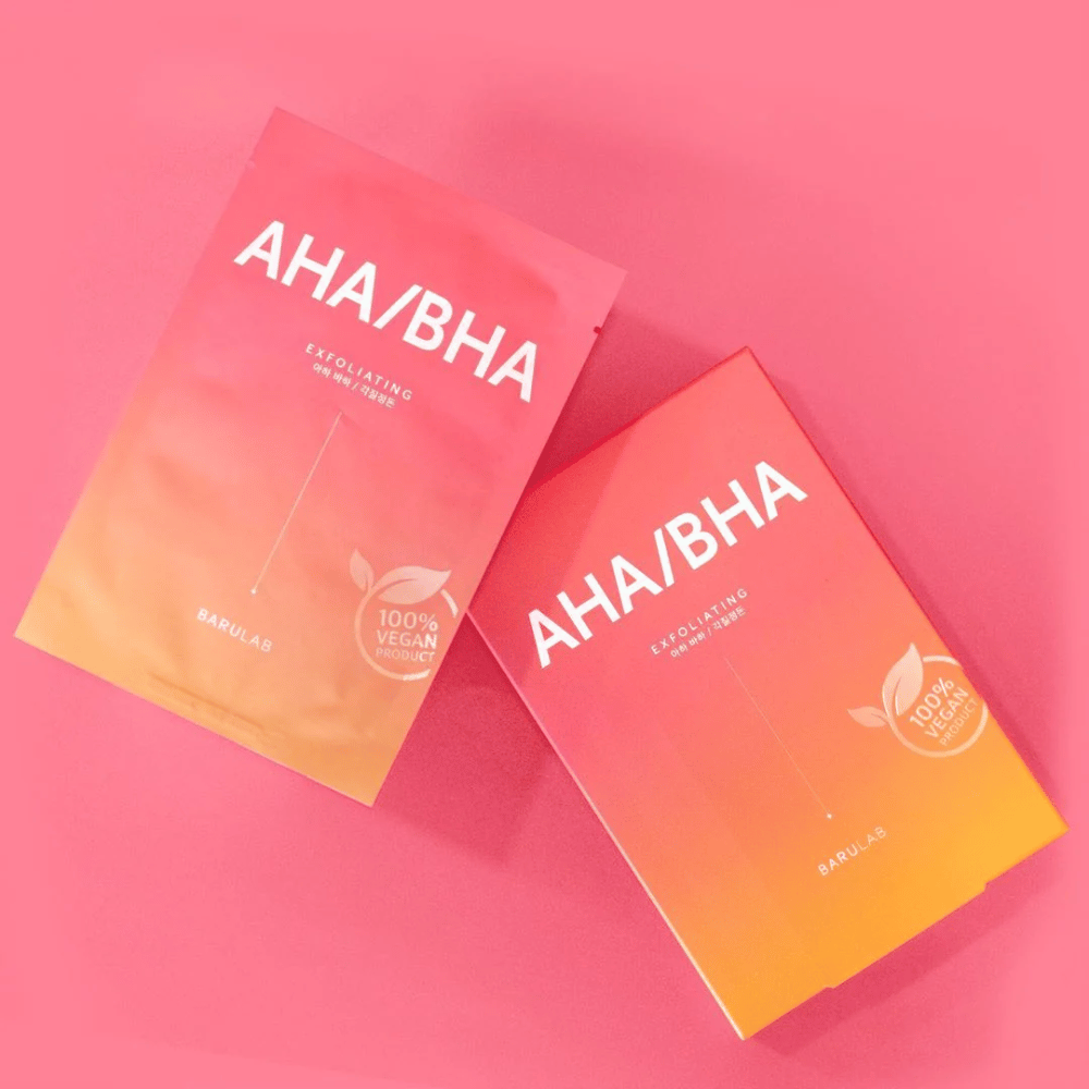 Twee producten van BARULAB, één in een zak en één in een doos, beide gemarkeerd met "AHA/BHA" en "Exfoliating" tegen een roze achtergrond. De producten zijn gemarkeerd als "100% Vegan Product".