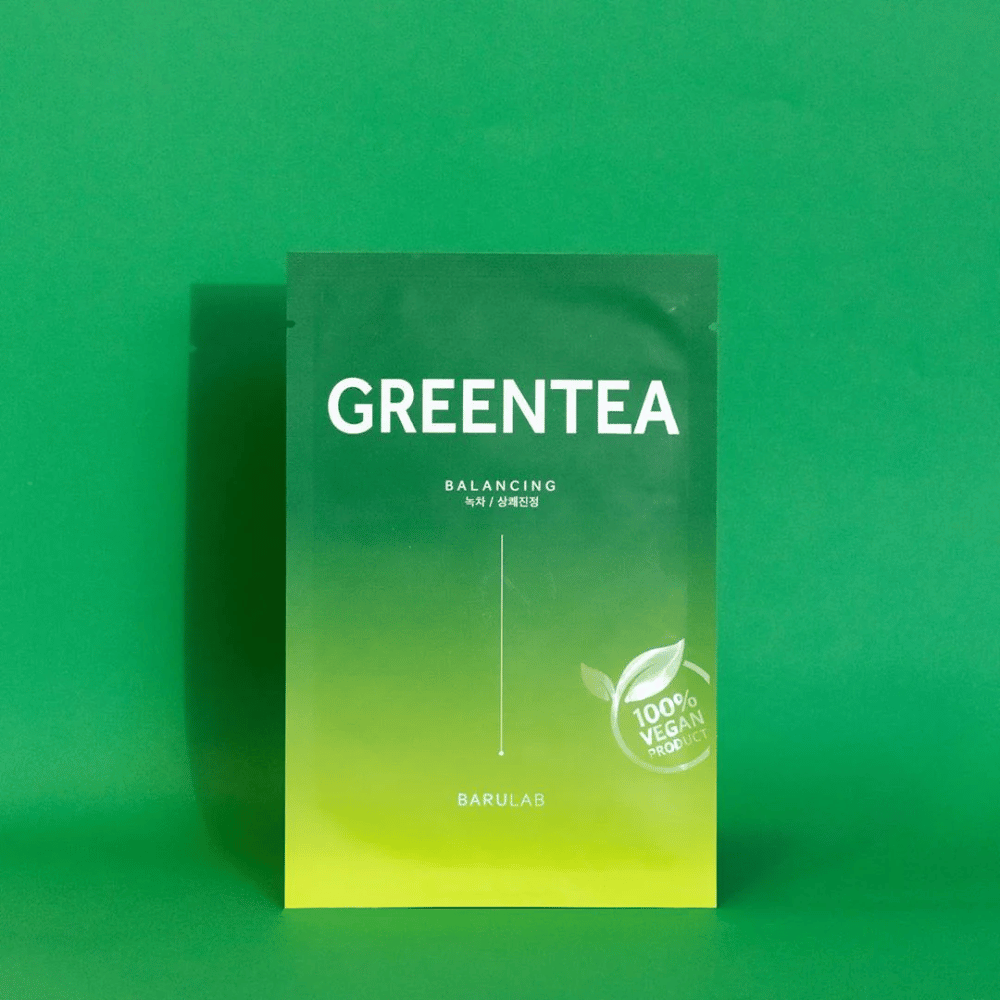 Een verpakking van BARULAB voor een "GREENTEA Balancing" masker, gemarkeerd als "100% Vegan Product". De kleur van de verpakking verloopt van donkergroen bovenaan naar lichter groen onderaan, tegen een uniforme groene achtergrond.