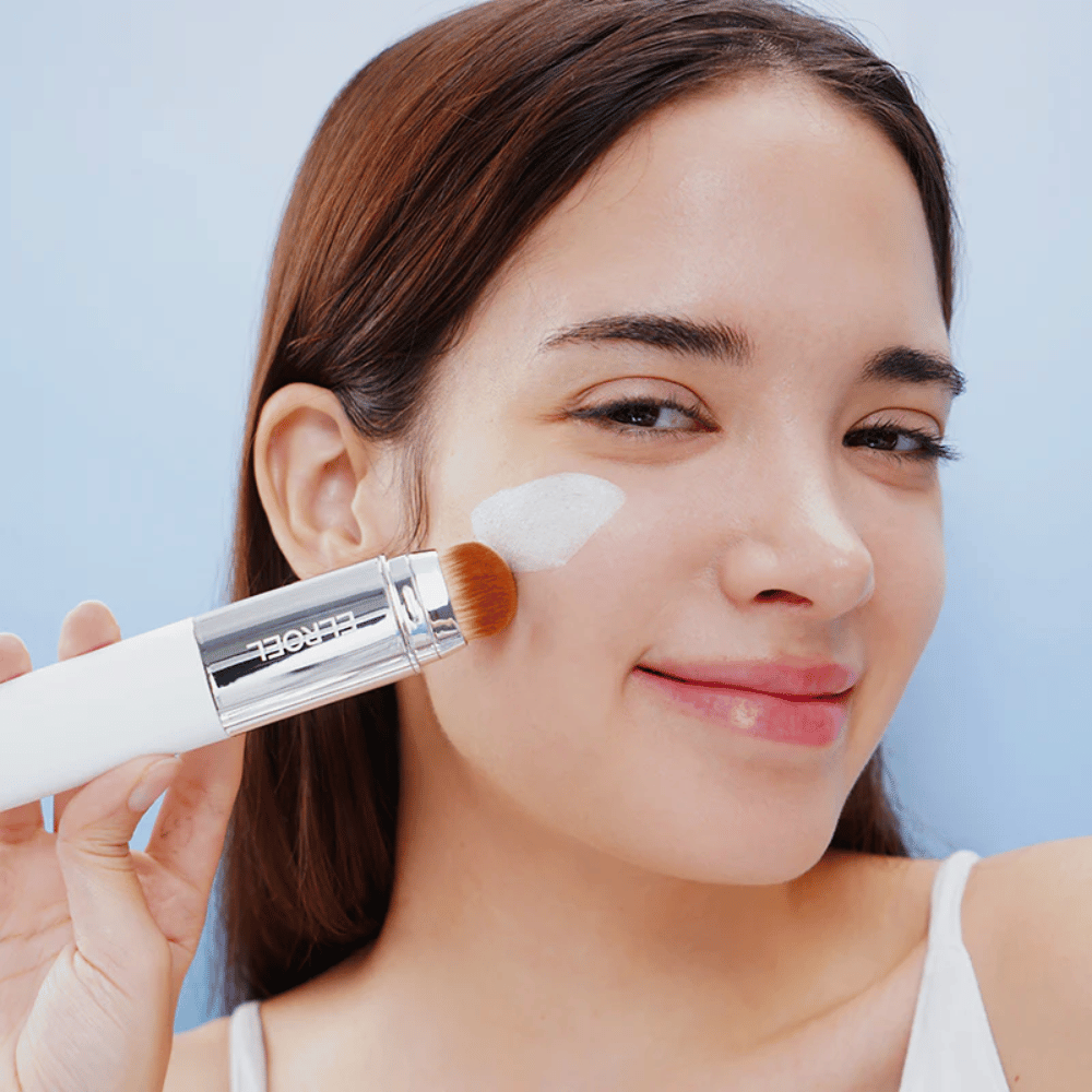 Model brengt ELROEL Blanc Cover Cream Stick concealer aan op de wang met ingebouwde borstel voor natuurlijke en egale dekking.