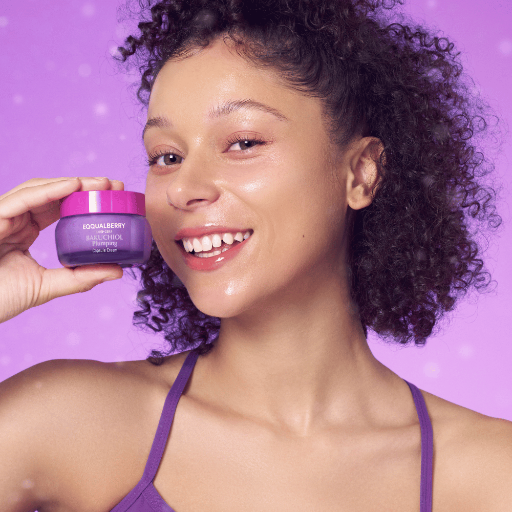Vrouw met stralende huid houdt EQQUALBERRY Bakuchiol Plumping Capsule Cream vast en glimlacht voor een paarse achtergrond.