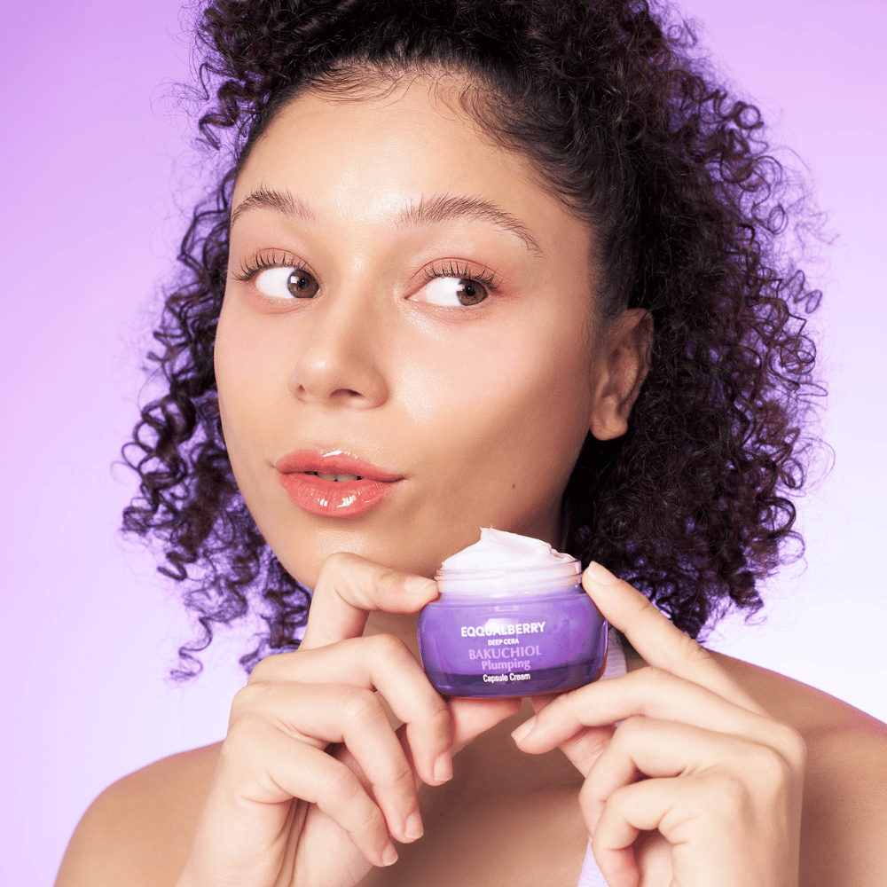 Vrouw houdt EQQUALBERRY Bakuchiol Plumping Capsule Cream in haar hand en toont haar gehydrateerde, stralende huid tegen een paarse achtergrond.