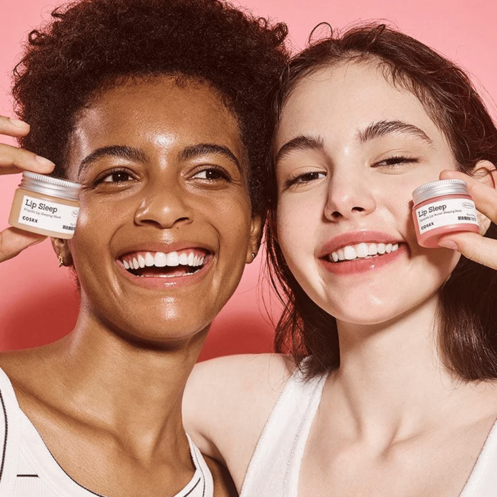 Twee personen glimlachen en houden COSRX Lip Sleep-potjes omhoog. De afbeelding geeft zachte, gehydrateerde lippen en het natuurlijke glow-effect van het product weer.