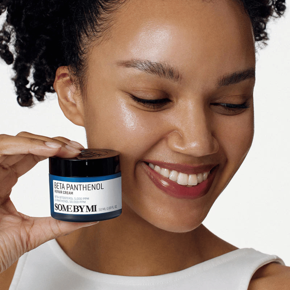 Model met glanzende huid houdt SOME BY MI Beta Panthenol Repair Cream vast – Koreaanse gezichtscrème die de huidbarrière versterkt en hydrateert.