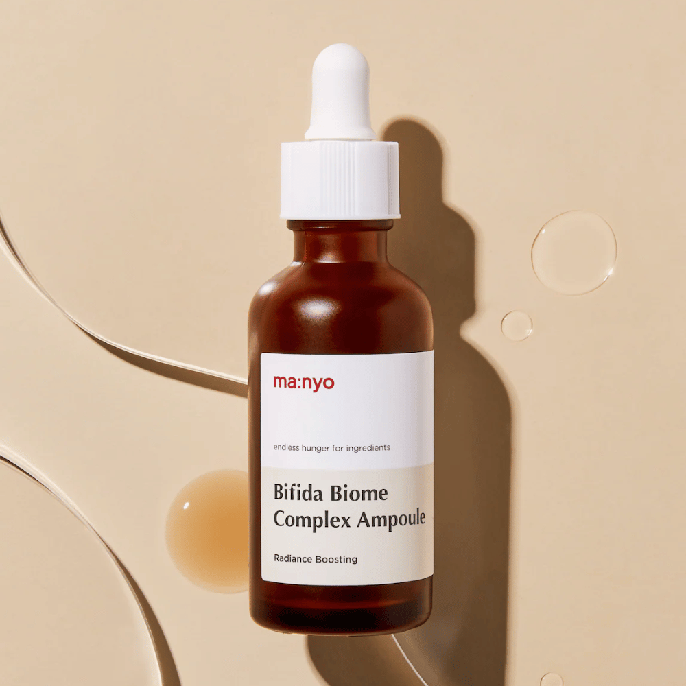 Strakke productafbeelding van ma:nyo Bifida Biome Complex Ampoule met focus op het flesontwerp en serumdruppels op de achtergrond.