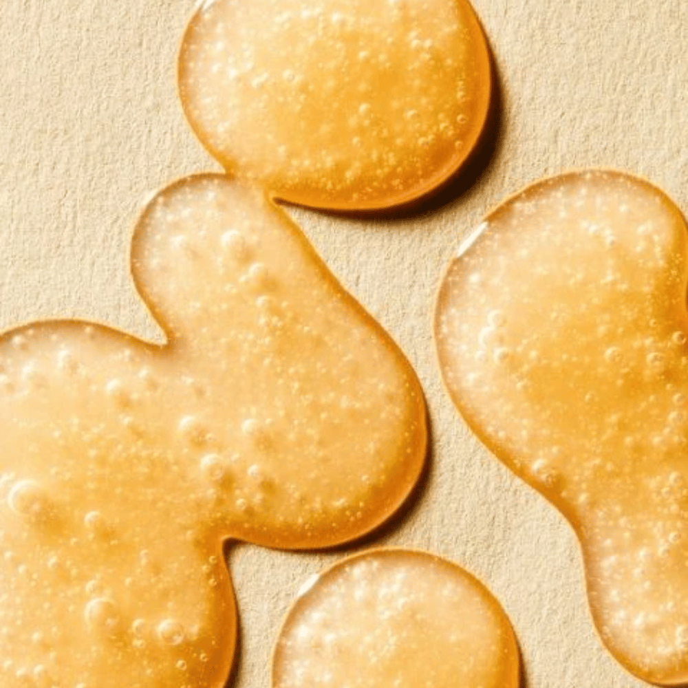 Textuurafbeelding die de gouden formule van het serum toont met kleine belletjes en een licht gelachtige consistentie.