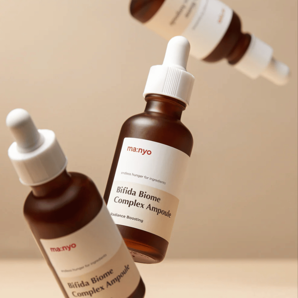 Productafbeelding met meerdere zwevende flessen van ma:nyo Bifida Biome Complex Ampoule tegen een beige achtergrond, wat een modern en minimalistisch gevoel geeft.