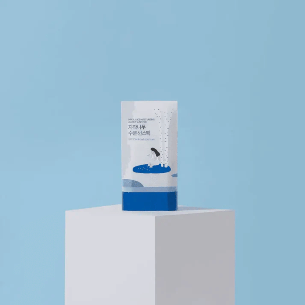 ROUND LAB Birch Juice Moisturizing Sun Stick SPF50+ staat op een sokkel tegen een blauwe achtergrond – hydraterende zonbescherming in stickvorm