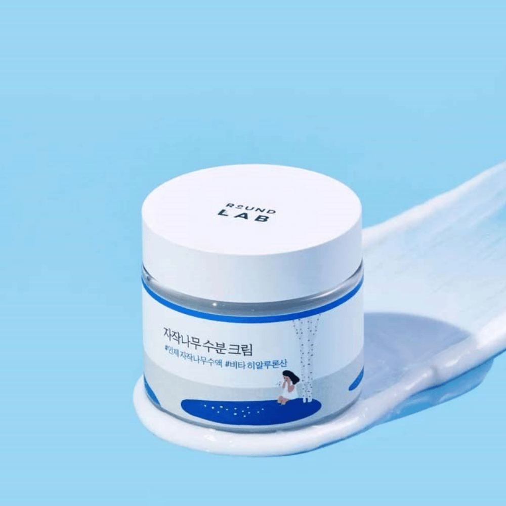 Round Lab Birch Juice Moisturizing Cream in blauwgetinte pot met wit deksel, staand in een laag crème tegen blauwe achtergrond.