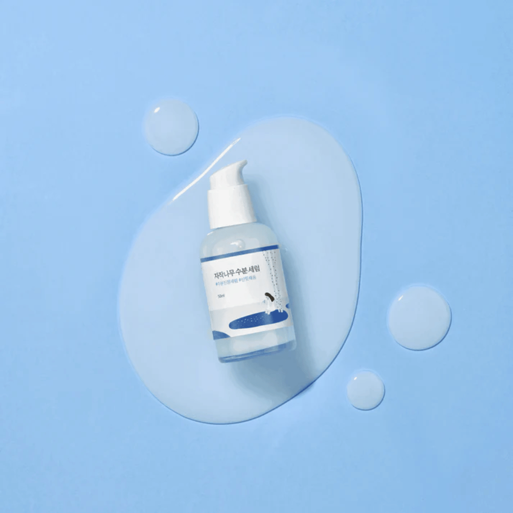 Round Lab Birch Juice Moisturizing Serum in doorzichtige pompflacon geplaatst op een blauwe achtergrond met druppels en gemorst serum.