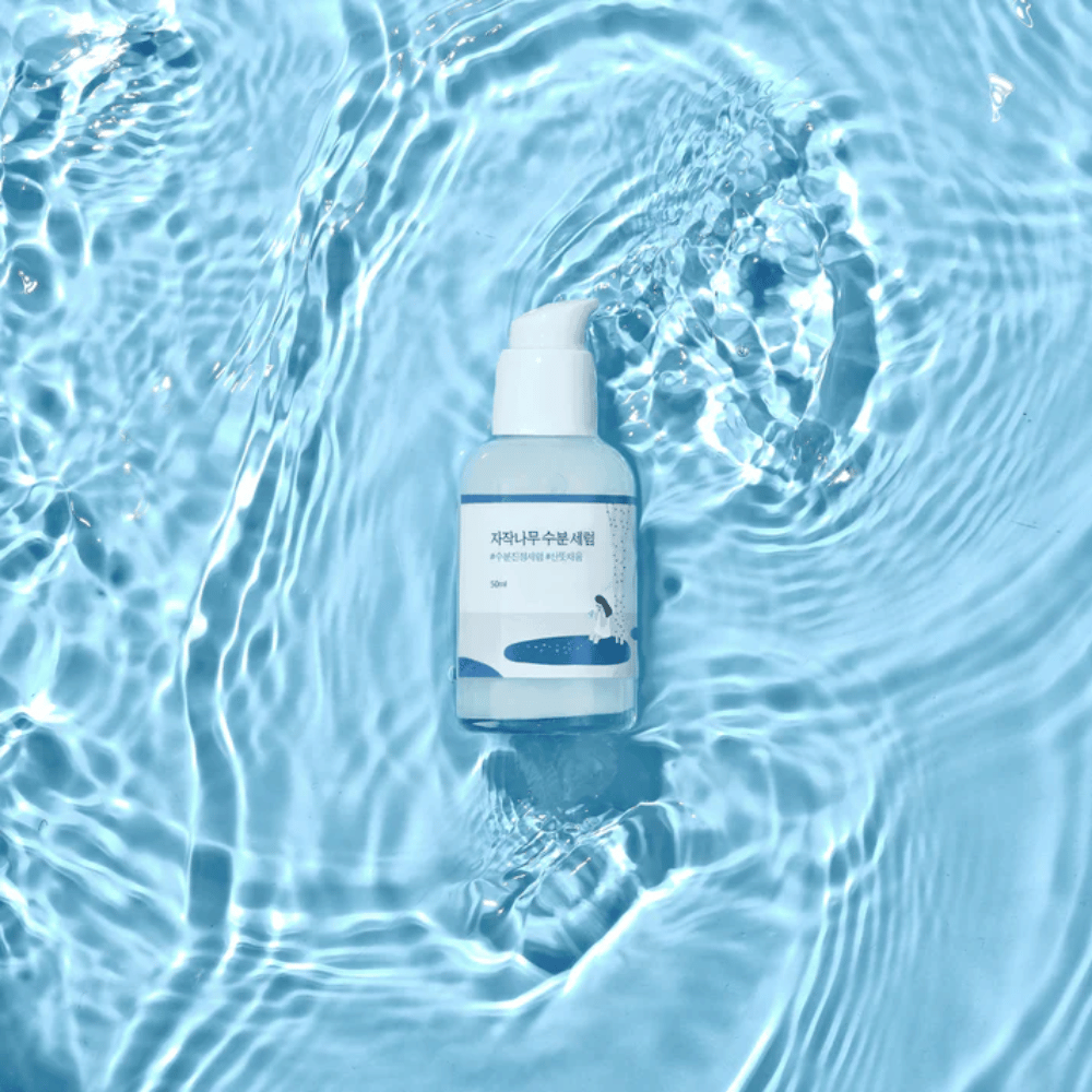 Round Lab Birch Juice Moisturizing Serum in pompflacon drijvend op blauw water met zonlichtreflecties.