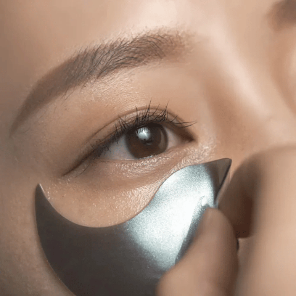 Gedetailleerde afbeelding waarop een zwarte hydrogel eye patch onder het oog wordt aangebracht. De afbeelding toont de nauwsluitende pasvorm en het verkoelende gevoel rond de oogzone.