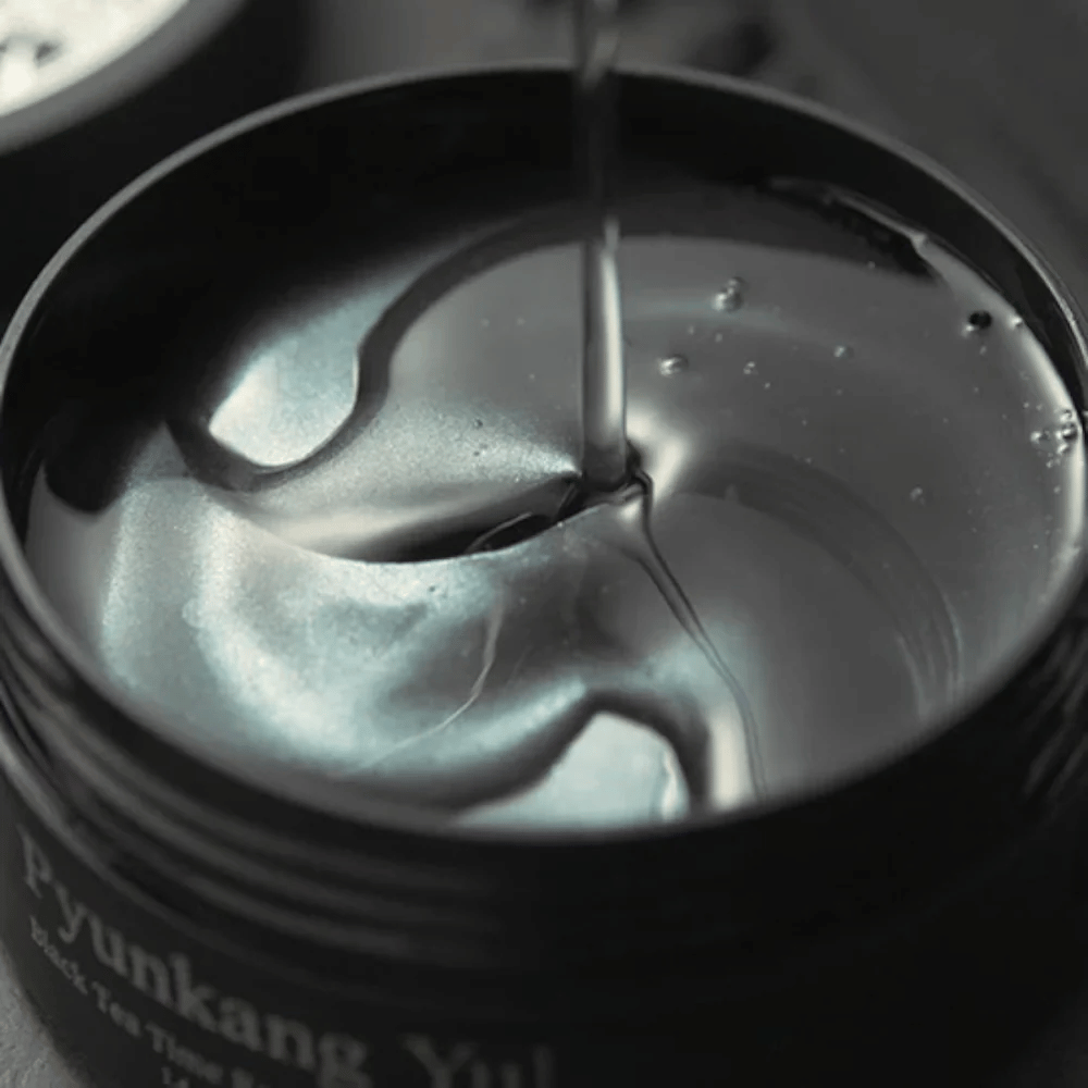 Close-up van zwarte hydrogel eye patches in een open pot van Pyunkang Yul. De glanzende patches liggen in serum en benadrukken het hydraterende en exclusieve gevoel van het product.