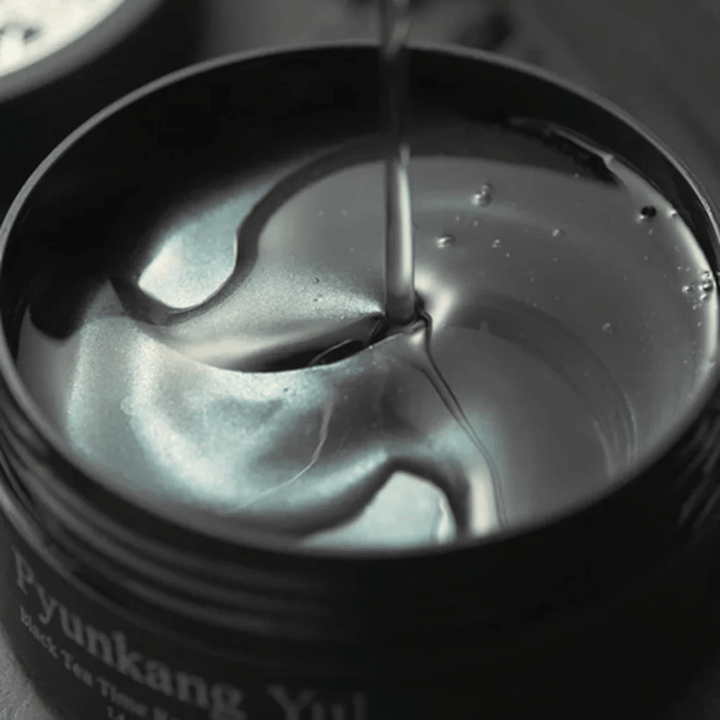 Close-up van zwarte hydrogel eye patches in een open pot van Pyunkang Yul. De glanzende patches liggen in serum en benadrukken het hydraterende en exclusieve gevoel van het product.