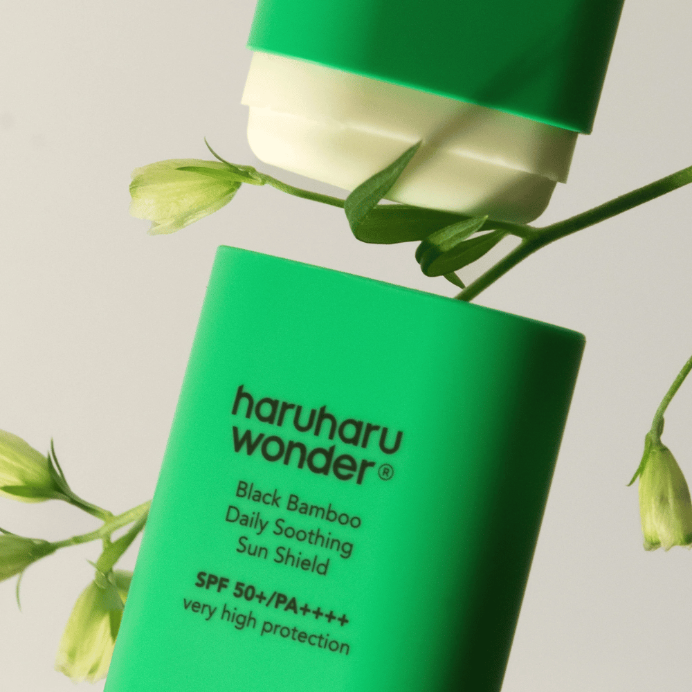 Close-up van Haruharu Wonder Black Bamboo Daily Soothing Sun Shield – een groene zonnebrand in stickvorm met SPF 50+ PA++++, omgeven door groene plantendetails.