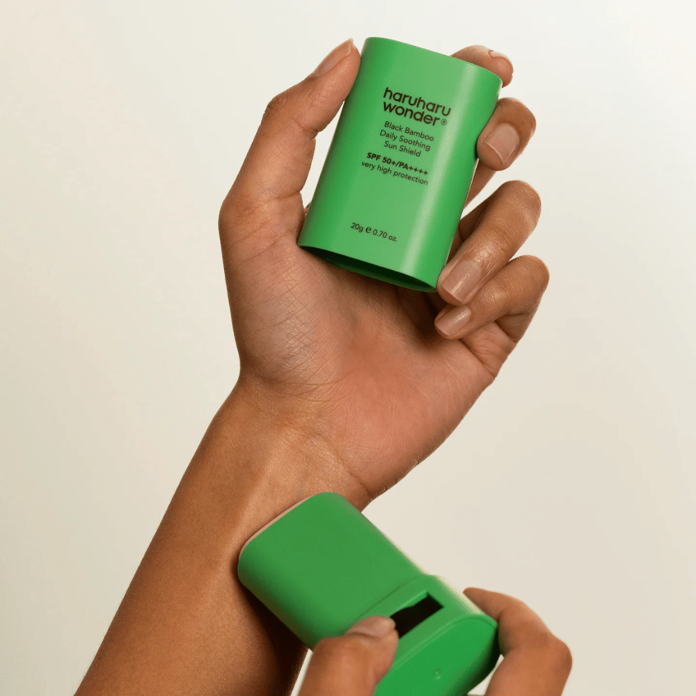 Een persoon brengt Haruharu Wonder Black Bamboo Daily Soothing Sun Shield – een groene zonnebrandstick met SPF 50+ PA++++ – aan op de pols.