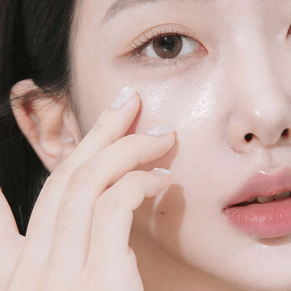 Close-up van een vrouw die oogcrème onder het oog aanbrengt met haar vingertoppen. De huid ziet er gehydrateerd, glanzend en verzorgd uit met een natuurlijke glans.