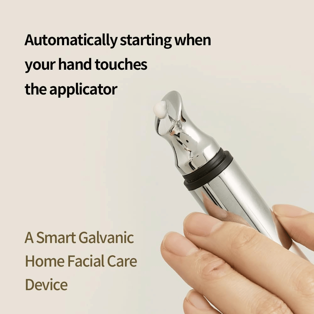 Close-up van een hand die een galvanische applicator voor oogcrème vasthoudt met automatische startfunctie bij aanraking. Tekst op de afbeelding beschrijft de functie en het apparaat als een slimme thuishulpmiddel voor gezichtsverzorging.