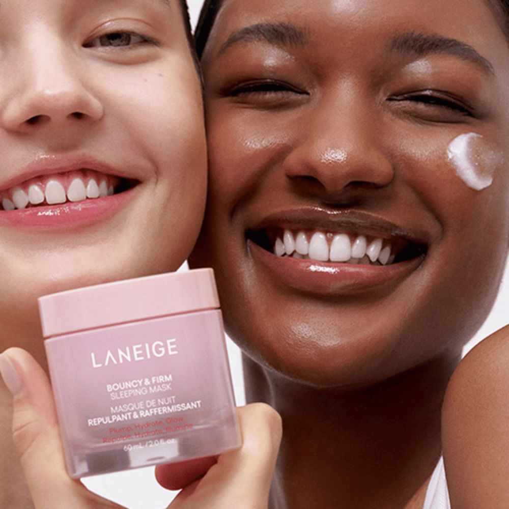 Twee personen lachen en houden Laneige Bouncy & Firm Sleeping Mask vast. De een heeft het masker op zijn wang aangebracht, en het product is duidelijk zichtbaar in hun handen. Het masker zit in een roze pot en wordt gepromoot als "Plump, Hydrate, Glow."