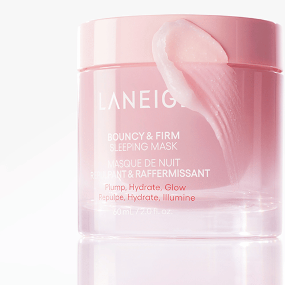 Close-up van Laneige Bouncy & Firm Sleeping Mask in een roze pot, met een deel van het masker dat op de rand van het deksel is aangebracht. Het product is bedoeld om volume, hydratatie en glans te geven. De pot bevat 60 ml en heeft de tekst "Plump, Hydrate, Glow."