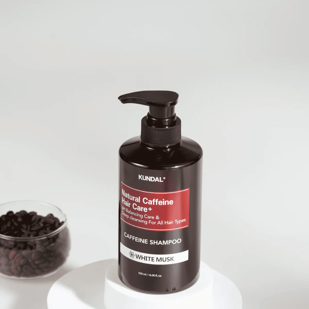 KUNDAL Natural Caffeine Hair Care+ Shampoo White Musk in zwarte pompfles, 500 ml, geplaatst naast een kom met koffiebonen.