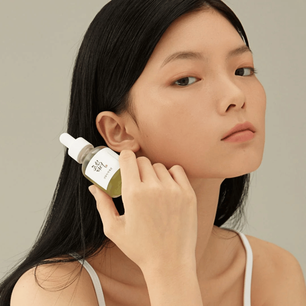 Model houdt Beauty of Joseon Calming Serum bij de wang – groene thee en panthenol die de huidbarrière versterken.