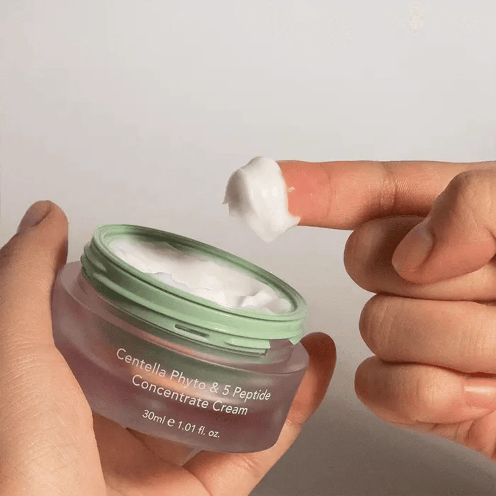 Hand die een klodder Centella Phyto & 5 Peptide Concentrate Cream uit een pot neemt.