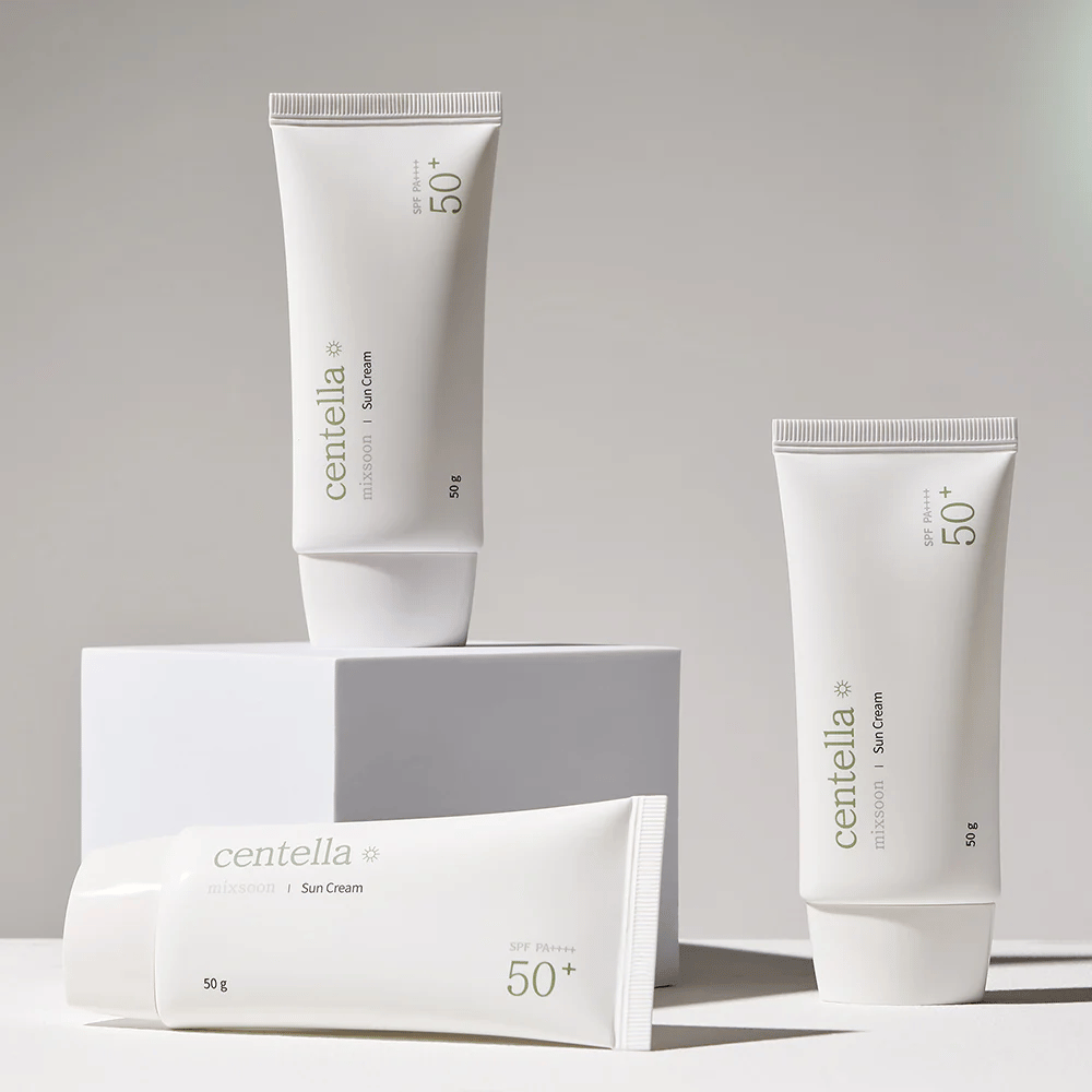 Drie verpakkingen van Centella Sun Cream SPF 50+ PA++++ esthetisch gerangschikt op witte podiums. Twee tubes staan rechtop en één ligt neer, allemaal met een witte, minimalistische vormgeving en groene tekstdetails.