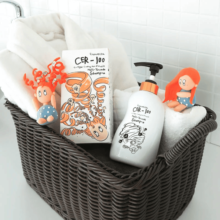 Presentatieafbeelding met Elizavecca CER-100 Shampoo en productverpakking geplaatst in een mand samen met handdoeken. Speelse figuren uit het verpakkingsontwerp benadrukken de unieke en creatieve stijl van het merk.