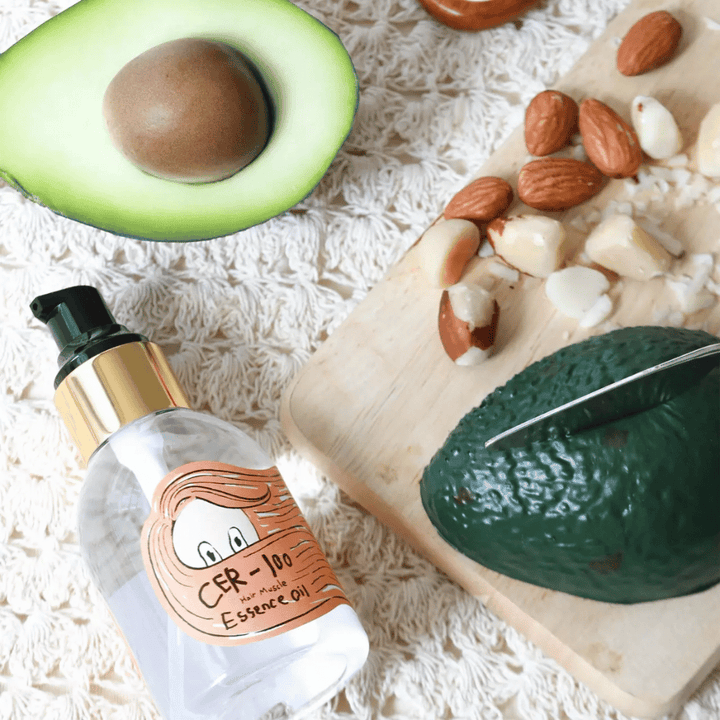 Elizavecca CER-100 Hair Muscle Essence Oil ingrediënten – close-up met avocado en plantaardige oliën die een voedende haarolie tonen die helpt het haar te verzachten en te verzorgen.