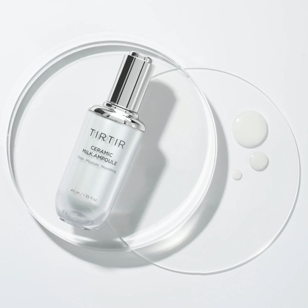 Een transparante fles TIRTIR Ceramic Milk Ampoule op een glazen plaat met druppels, tegen een witte achtergrond, benadrukt glans, vocht en voeding.