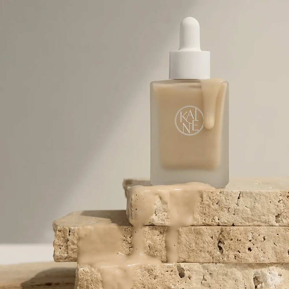 KANE Chaga Collagen Charging Serum in een matglazen fles met pipet. Romige textuur stroomt over natuurlijke stenen in een zacht en minimalistisch licht.