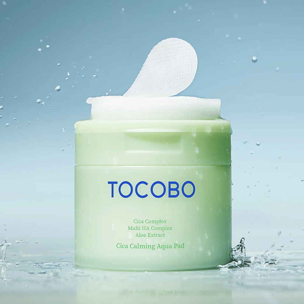 Open pot met TOCOBO Cica Calming Aqua Pad waarbij een tonerpad uit de verpakking steekt. Waterdruppels rond het product versterken het gevoel van intensieve hydratatie en frisheid.