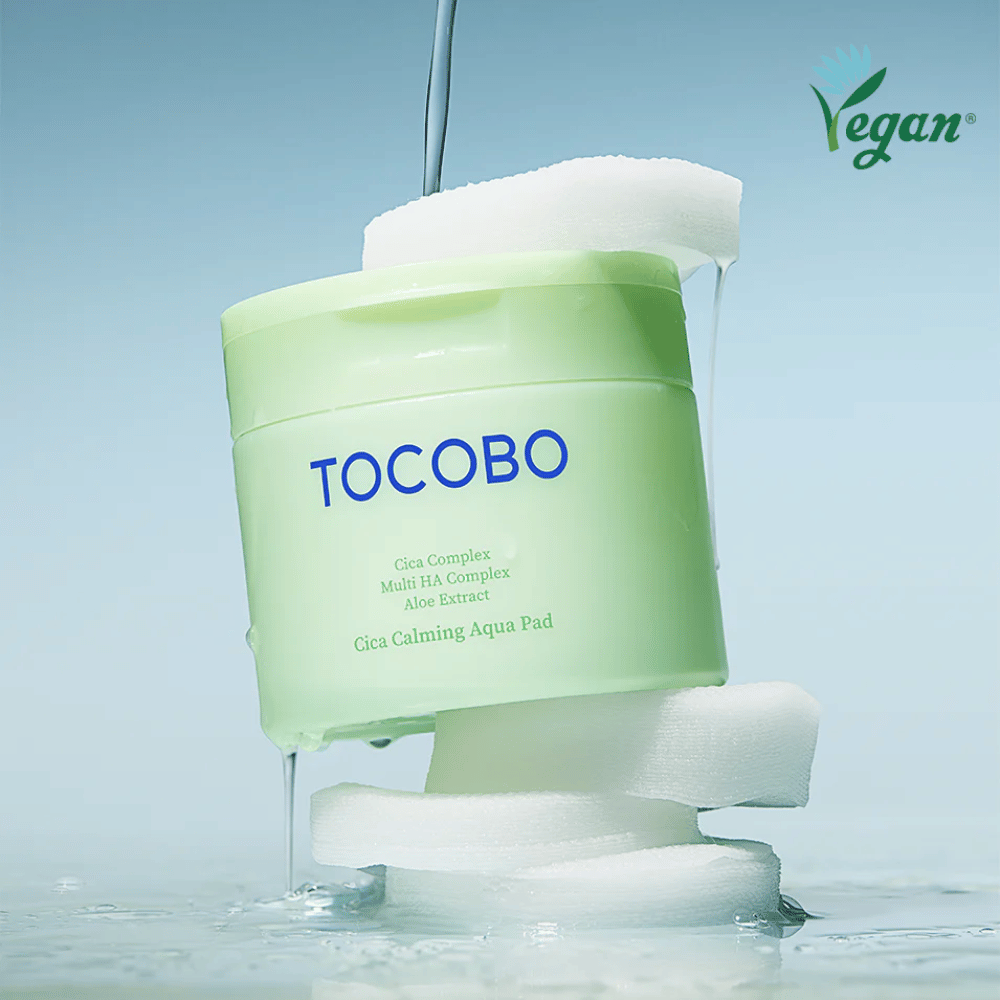 TOCOBO Cica Calming Aqua Pad geplaatst tussen tonerpads met stromende essence. Het vegan-symbool benadrukt de veganistische formulering van het product en het huidvriendelijke profiel.