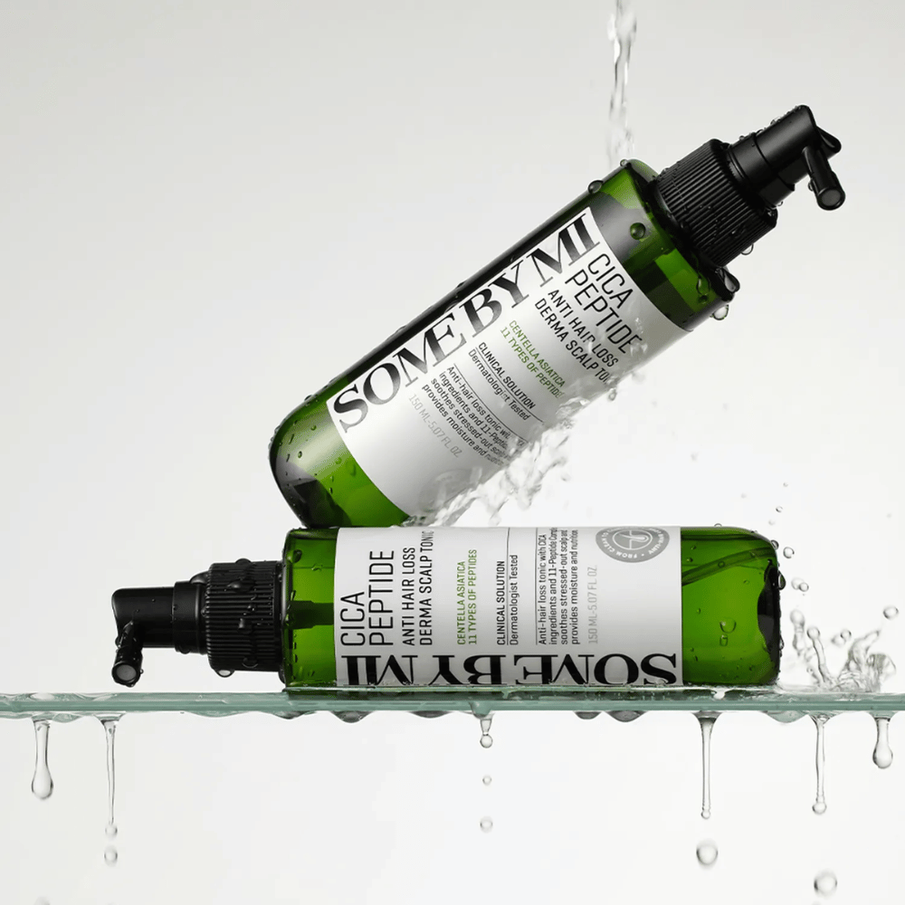 Twee flessen SOME BY MI Cica Peptide Anti Hair Loss Derma Scalp Tonic liggen in en boven water met spetters, groene flessen met zwart spuitmondstuk en wit etiket.