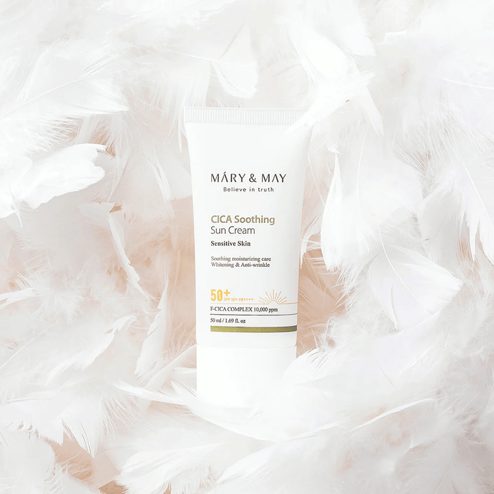 Mary&May CICA Soothing Sun Cream omringd door zachte witte veren. De afbeelding brengt een gevoel van zachtheid, comfort en een lichte formule over, afgestemd op de gevoelige huid.