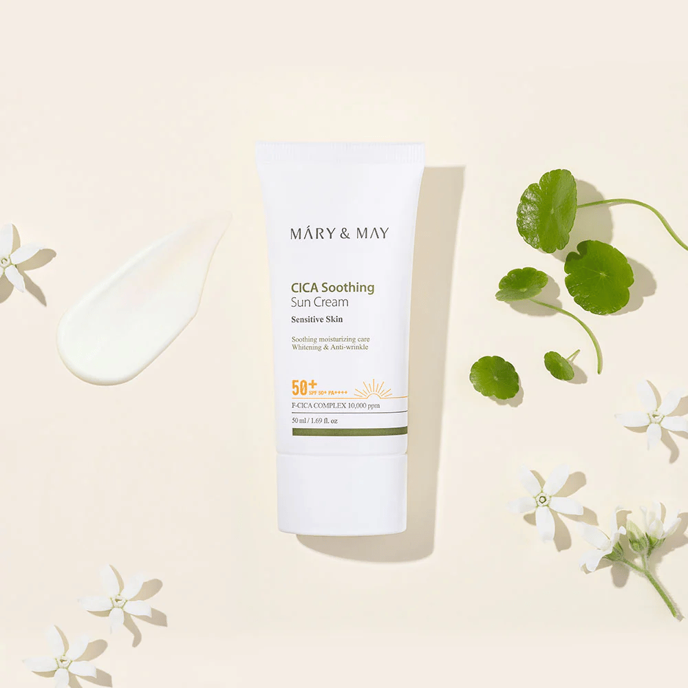 Mary&May CICA Soothing Sun Cream SPF50+ PA++++ gepresenteerd samen met een crèmeachtige textuur, centella-bladeren en witte bloemen. De afbeelding benadrukt de kalmerende eigenschappen van het product en de focus op de gevoelige huid.