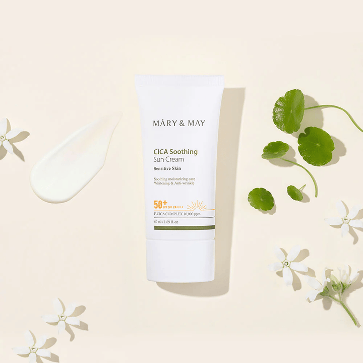Mary&May CICA Soothing Sun Cream SPF50+ PA++++ gepresenteerd samen met een crèmeachtige textuur, centella-bladeren en witte bloemen. De afbeelding benadrukt de kalmerende eigenschappen van het product en de focus op de gevoelige huid.