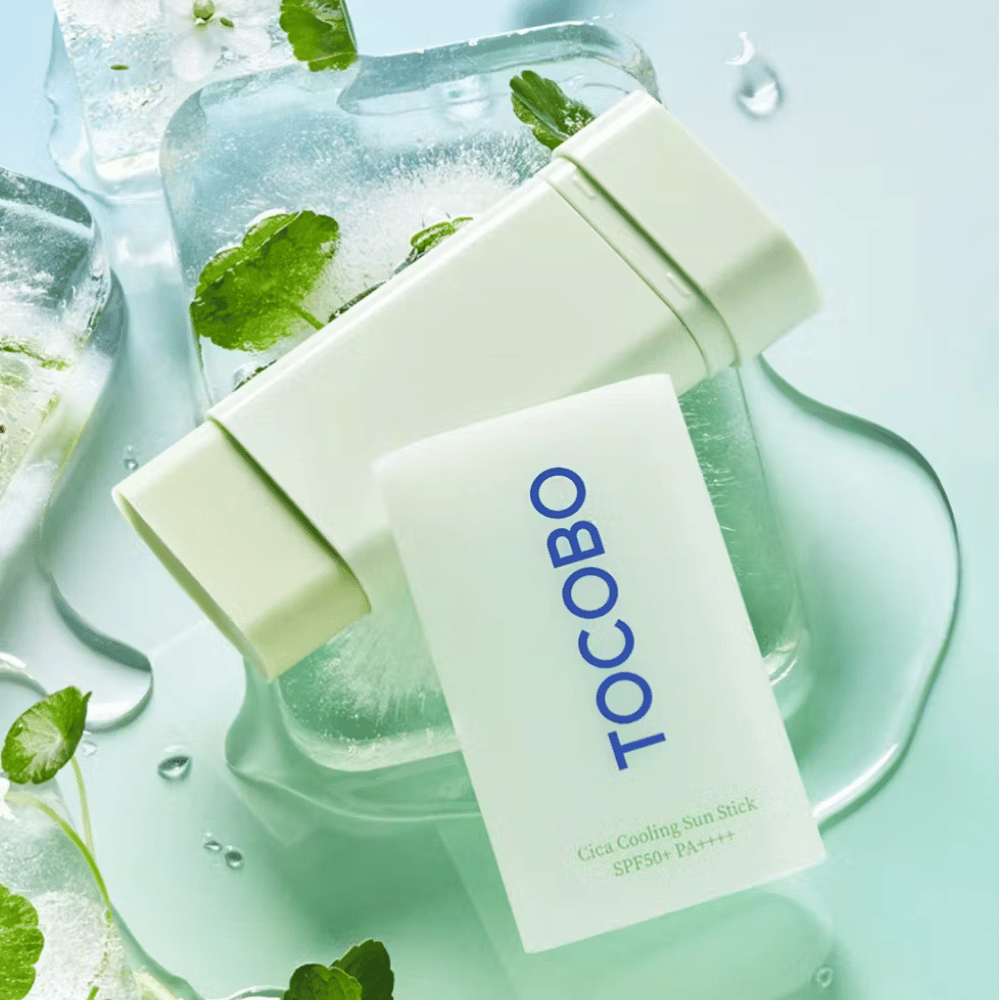 Tocobo Cica Cooling Sun Stick SPF50+ PA++++ op ijsblokjes met groene plantbladeren, wat een verkoelend en verfrissend gevoel overbrengt.
